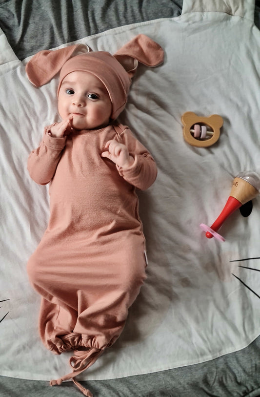 Baby in baby pink sleep gown and sweet bunny hat, lying on a play mat