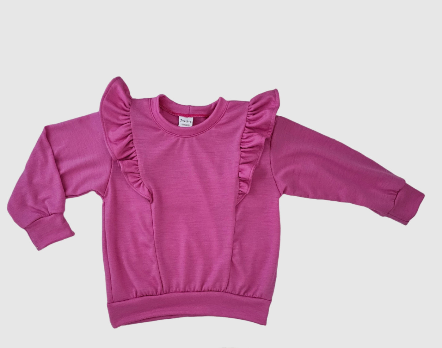 Pink sweatshirt with ruffled sleeves on a wooden surface