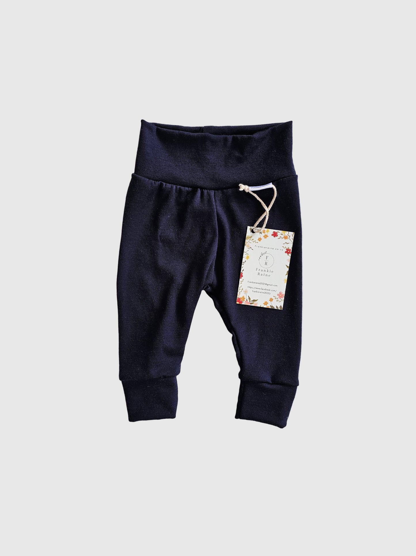 Navy blue baby pants with a tag on a light gray textured surface