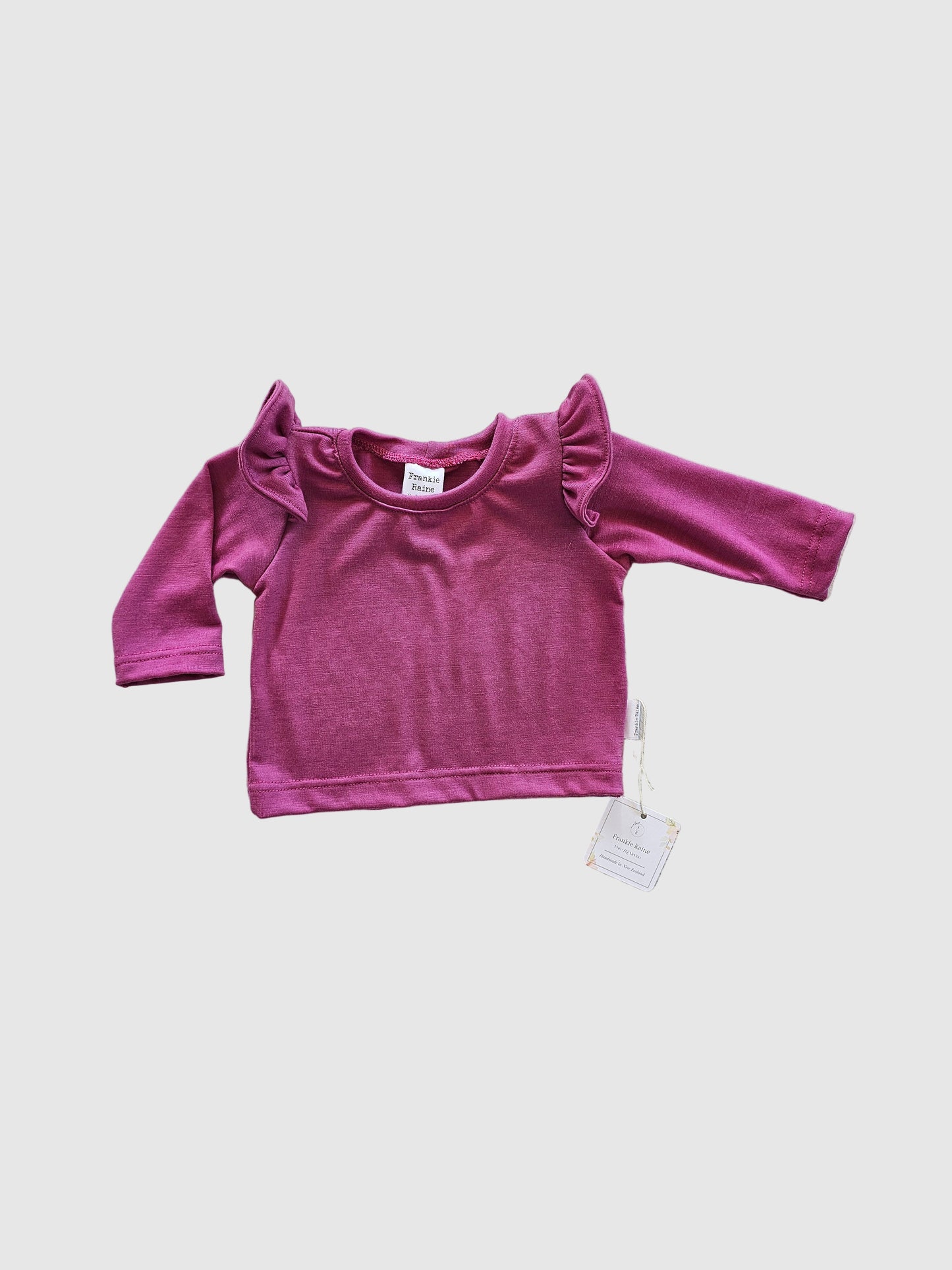 Purple long-sleeve top with a tag on a light gray surface