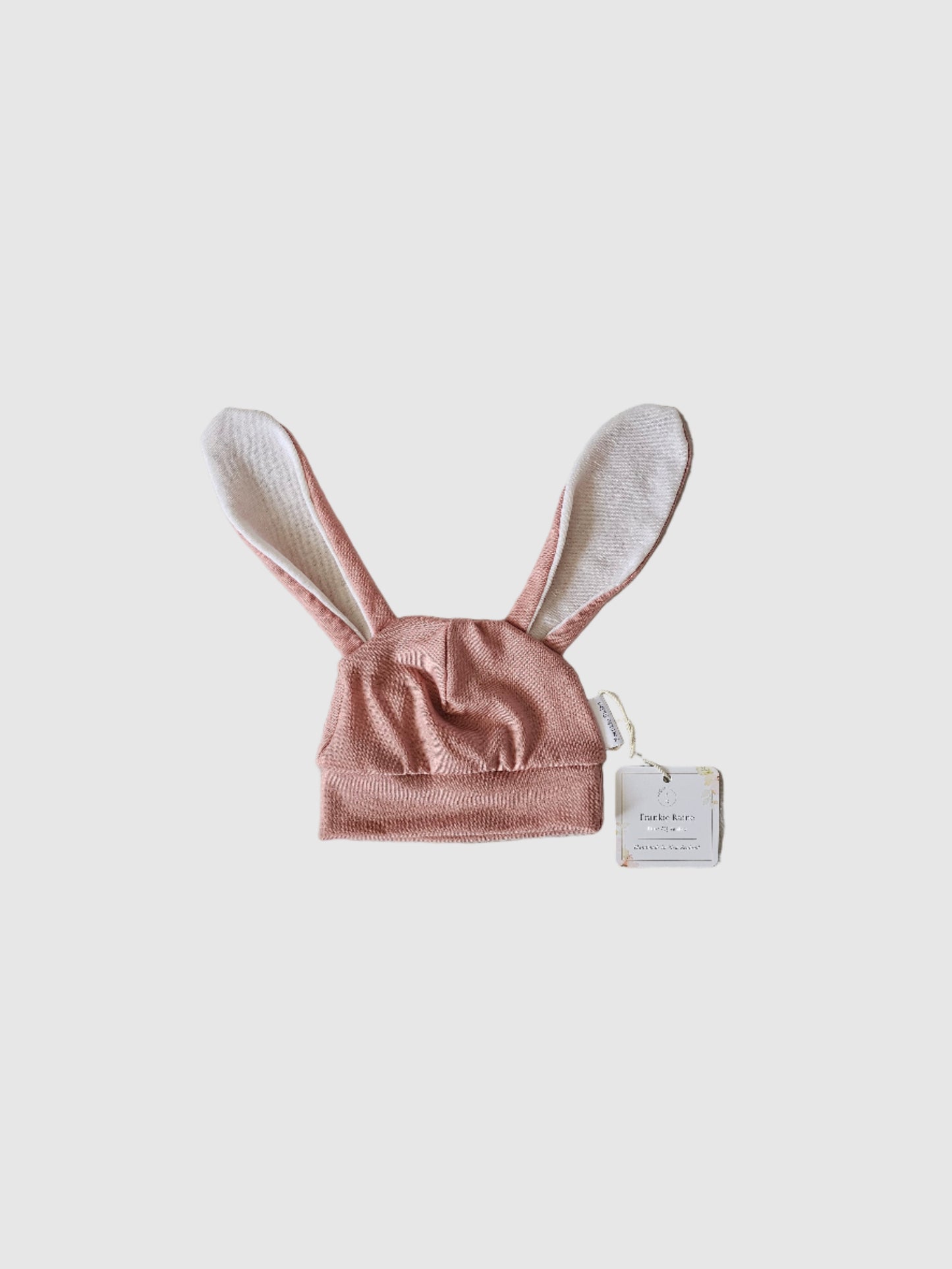 Pink bunny ears headband with a tag on a textured gray surface