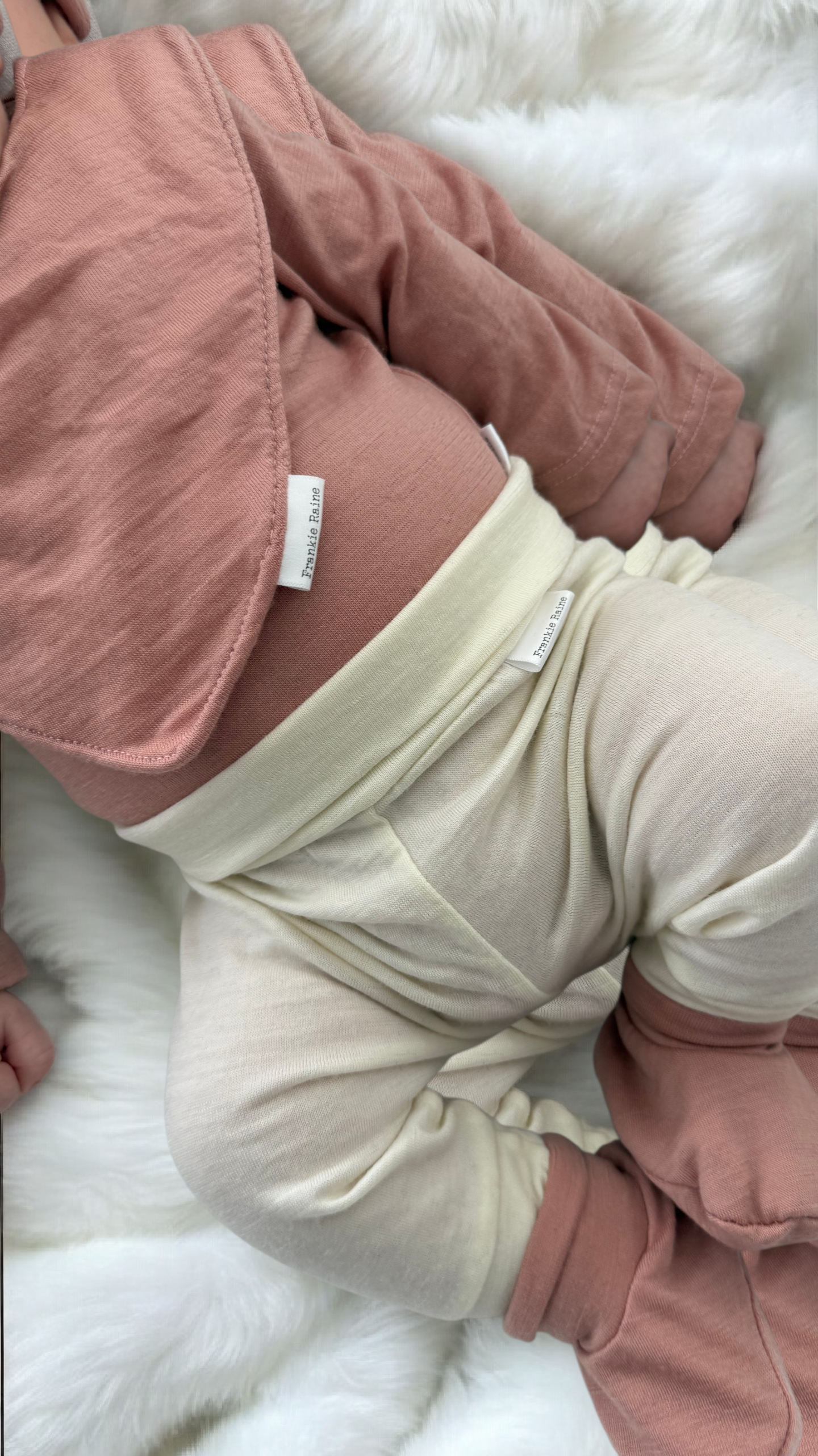 Merino baby leggings in Ivory with booties, bodysuit, and bib in Vintage Blush, worn by baby on white background.