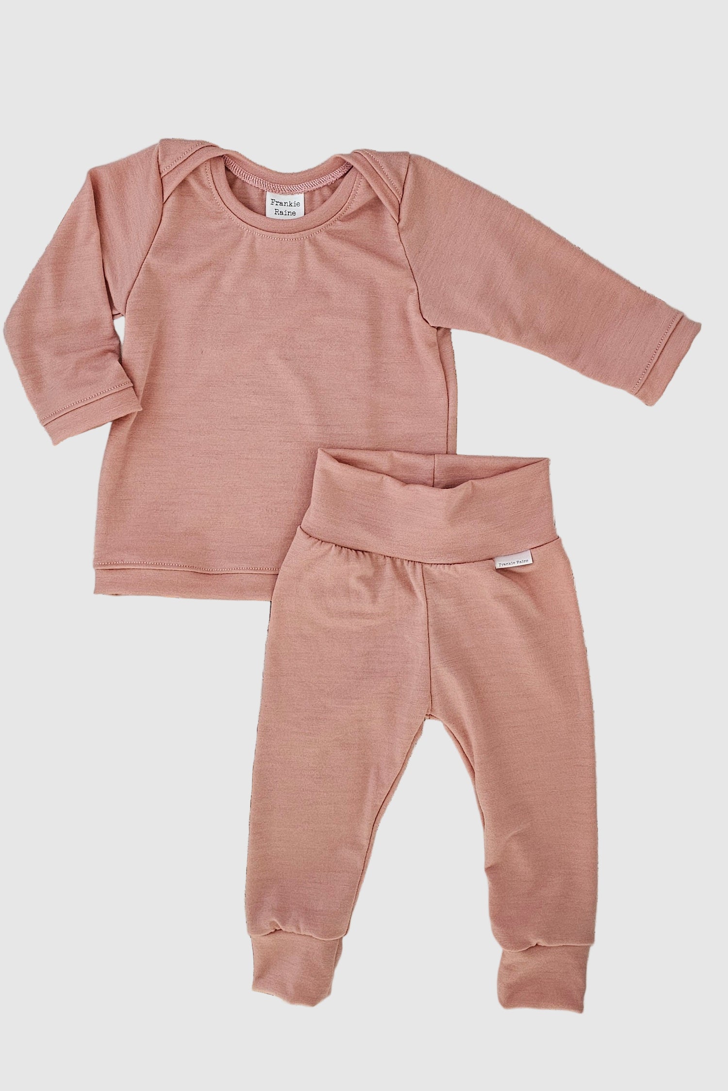Pink baby outfit with long-sleeve top and pants on a wooden surface