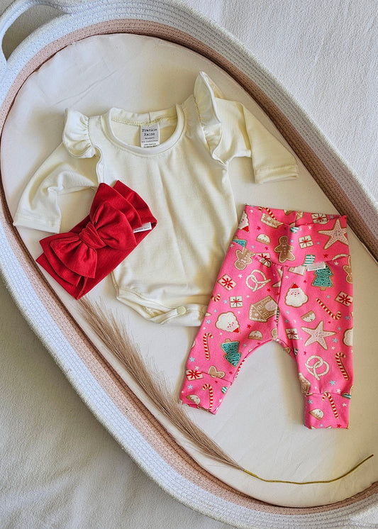 Baby clothes including a pink outfit, white onesie, and red headband on a heart-shaped cushion.
