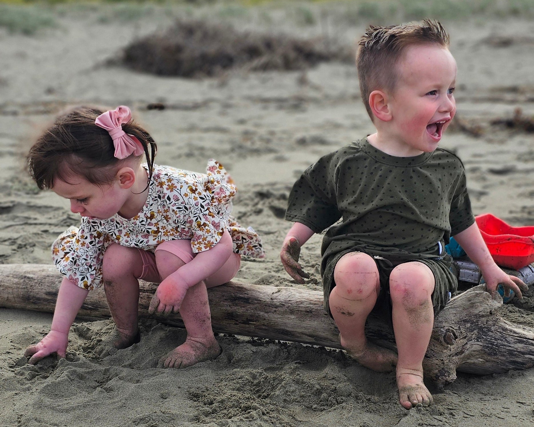 Two children playing in the sand on a beach with a cloudy sky.