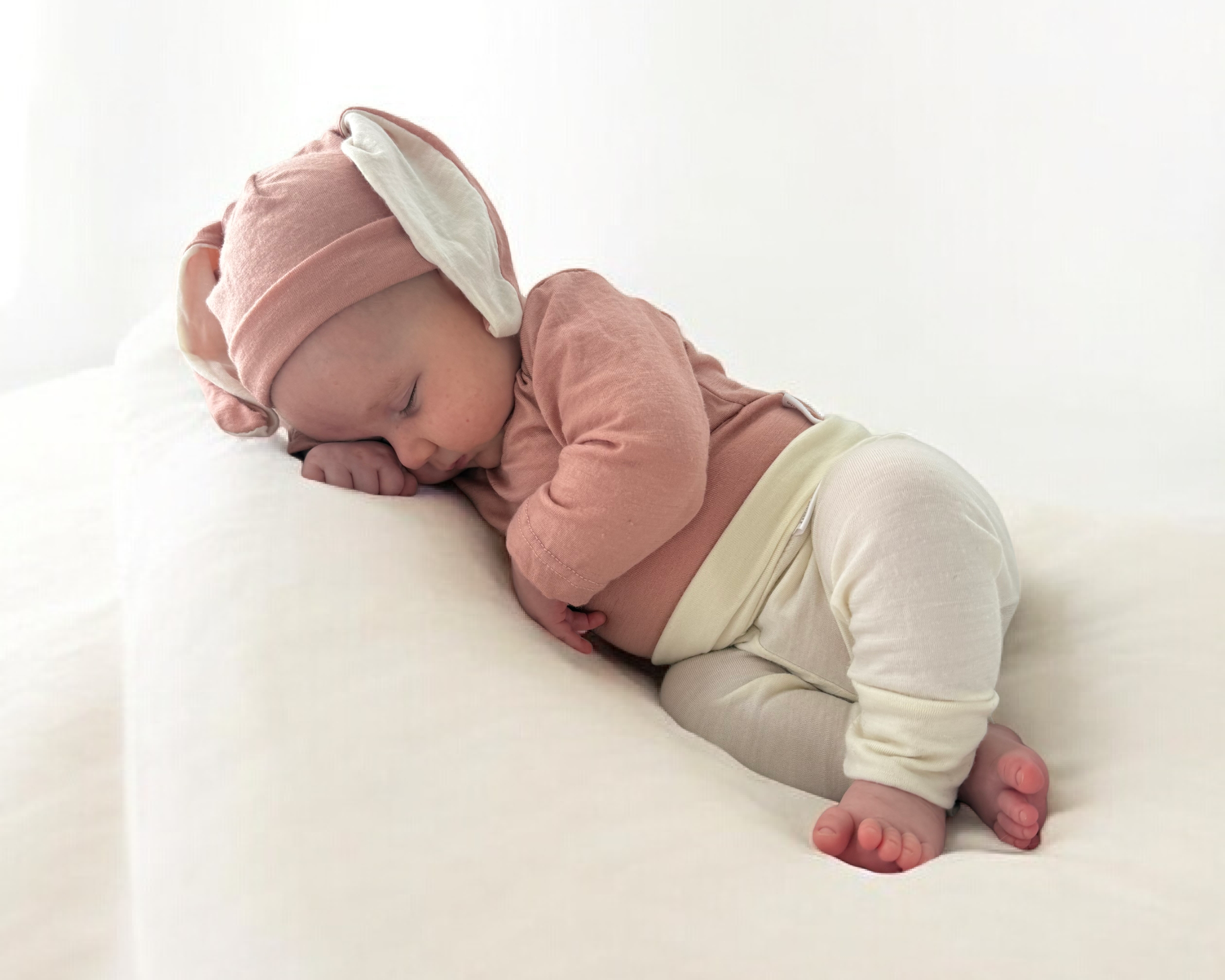 Baby in pink outfit and white pants lying on a white surface
